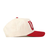The No Rivals Utah Utes Stride Hat, shown in profile view, features a white crown with a red visor and partially visible large red and black embroidered logos on the front panel.