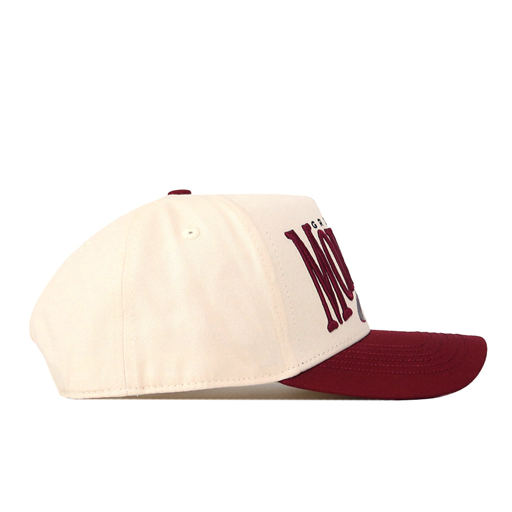 The No Rivals Montana Grizzlies Stride Hat is a cream-colored snapback cap with a maroon brim and partially visible maroon text on the front. Featuring a classic gameday fit, the hat is shown from the side against a white background.