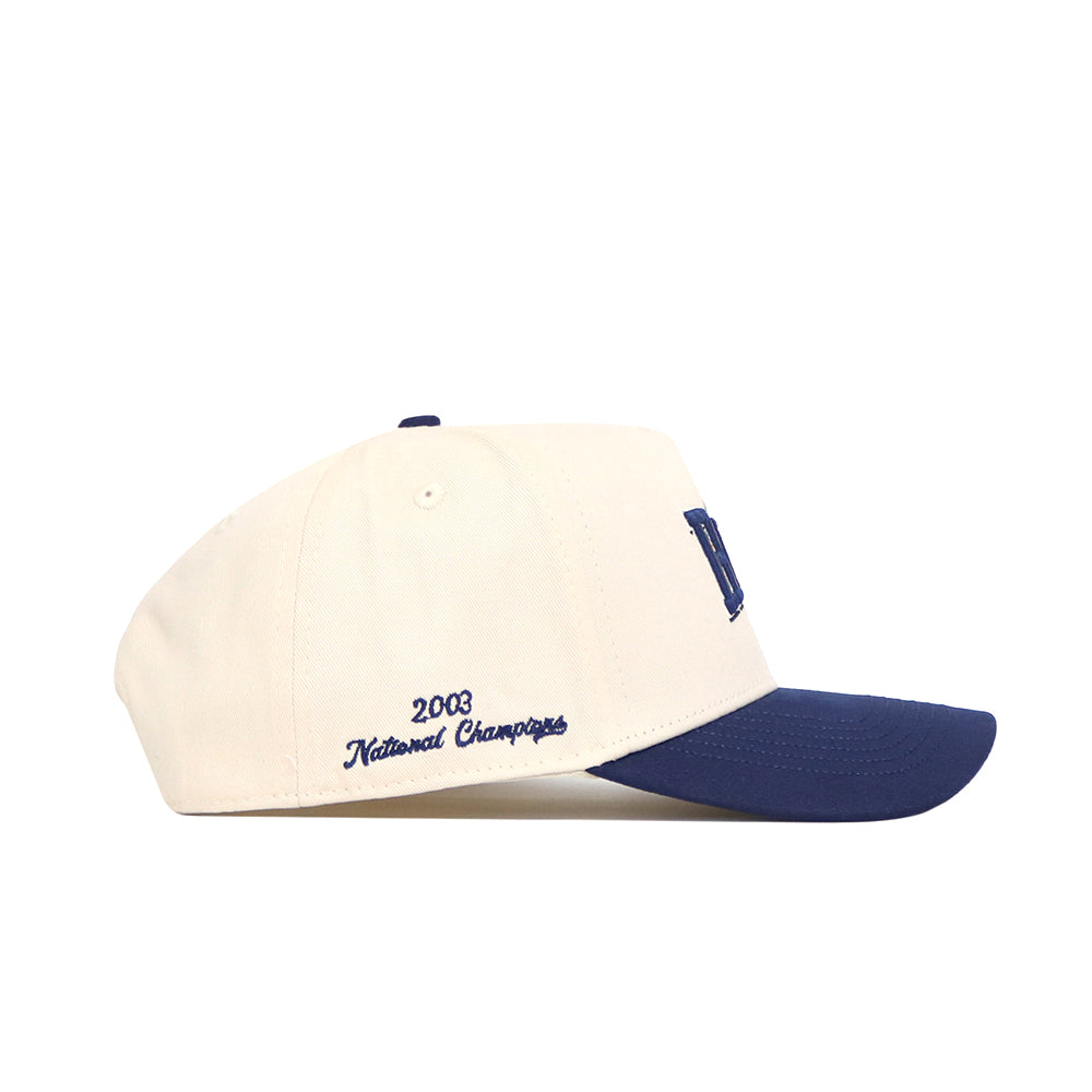 The Rice Ballpark Hat by No Rivals is a cream baseball cap with a navy bill, adjustable snap back, and blue "2003 National Champions" embroidery on the side.
