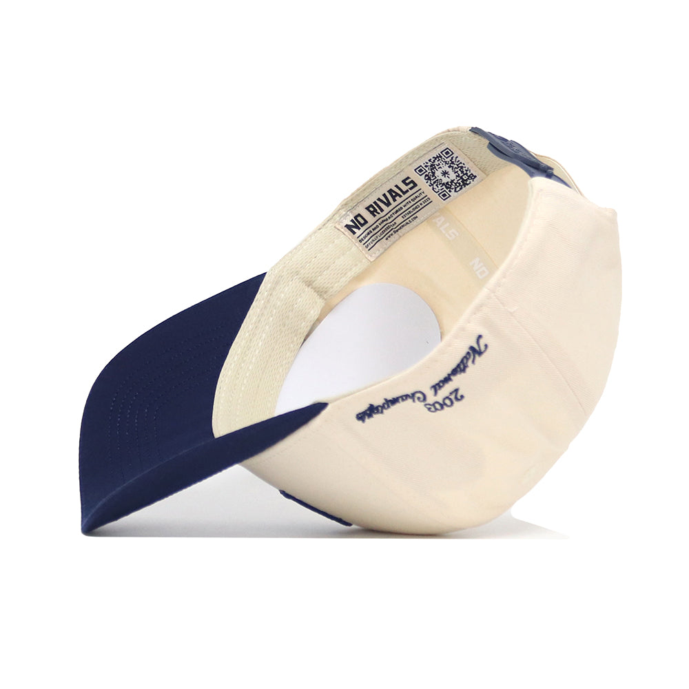 The Rice Ballpark Hat by No Rivals is shown upside down, displaying its beige/navy colors, snap back, inside lining, a stitched 2023 National Champions message on the brim, a QR code, NO RIVALS tag, and embroidered logo.