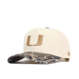 The Miami Camo Connector Hat by No Rivals features a structured fit in high-quality cotton, a beige crown with a large gold U embroidered on the front, and a camouflage-patterned curved brim.