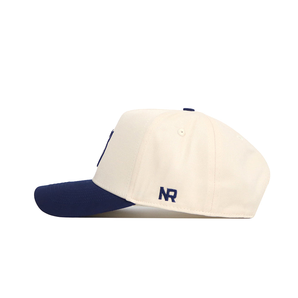 The Rice Sammy Sailor Patch Hat by No Rivals is a cream snapback with a navy brim and a small official NR logo on the left. The cap is pictured in profile against a plain white background.