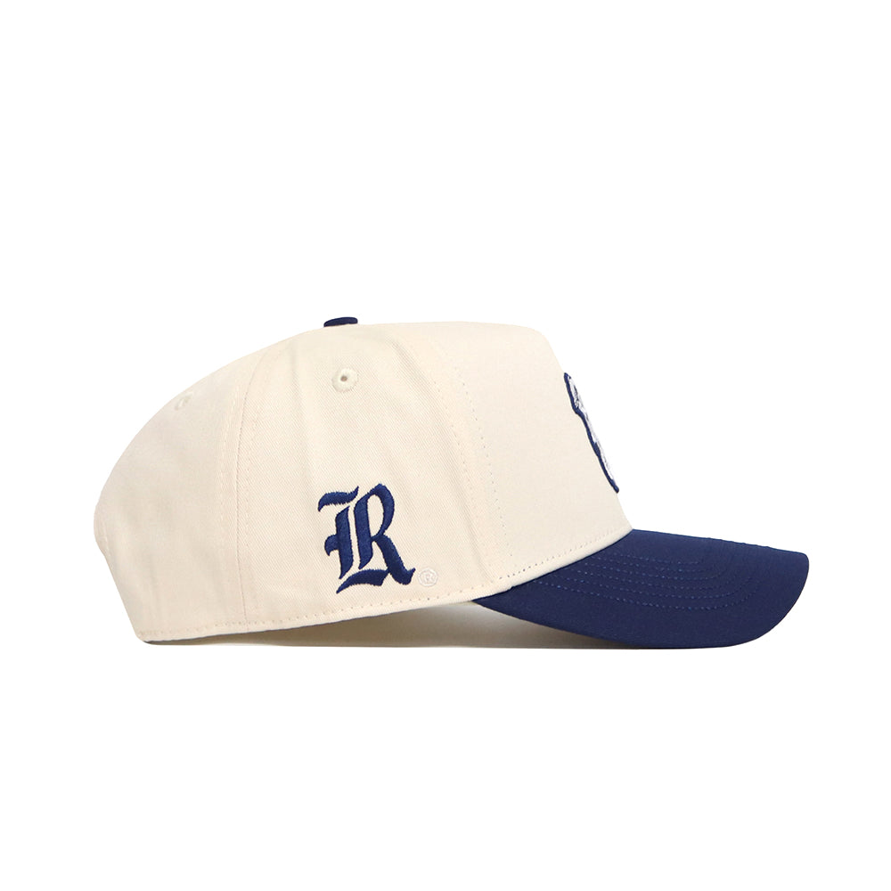 The No Rivals Rice Sammy Sailor Patch Hat is a cream snapback with a navy brim, featuring an officially licensed stylized blue "R" embroidered on the side.