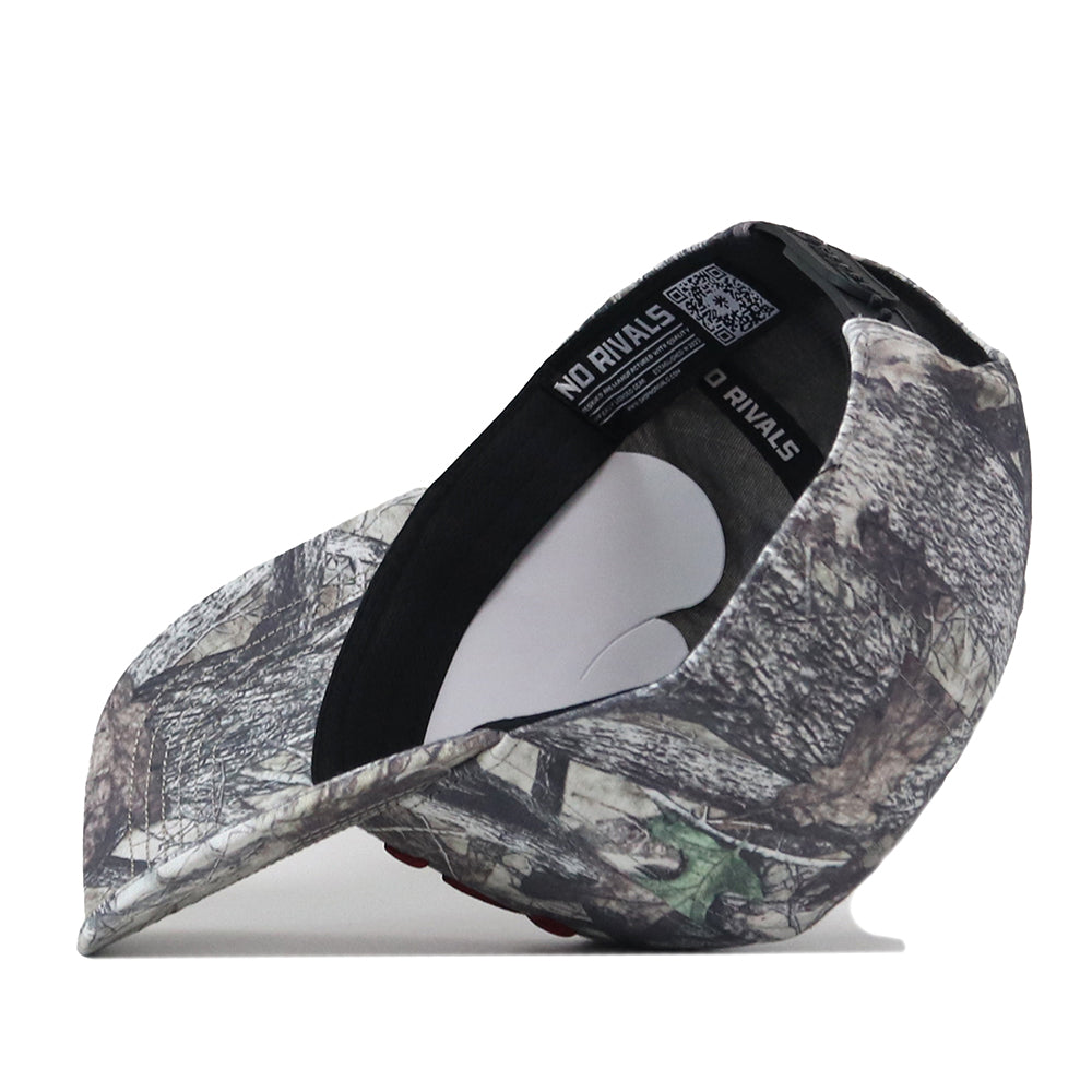 The Troy Outland Hat by No Rivals, a camouflage baseball cap with a snap back adjustment, is flipped upside down to reveal the inner lining and tags featuring the NO RIVALS text. The cap rests on a white surface.