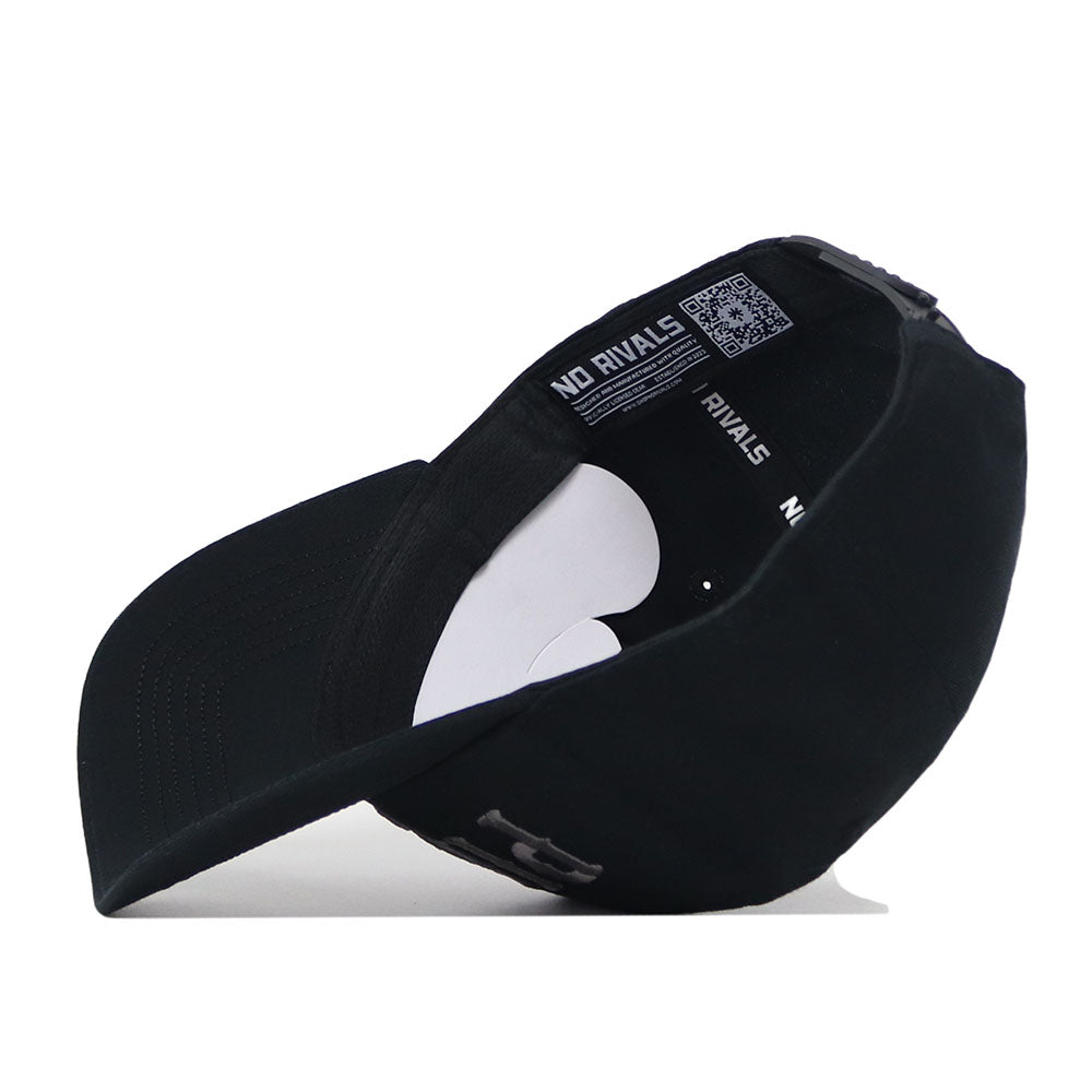 The ECU Pirates Night Mode Hat by No Rivals is displayed upside down, revealing the inside with "NO RIVALS" text on the inner band and a QR code on the label. Made from high-quality cotton for comfort and durability, this black snapback features a curved brim and an adjustable strap at the back for a structured fit.