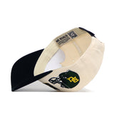 The Baylor Alma Mater Hat by No Rivals is a cream baseball cap with a black brim, shown from an angled underside. It features a structured snapback fit, an inside NO RIVALS label, and part of a green football helmet with gold letters on the side.