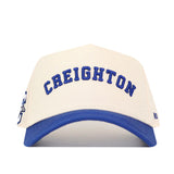 The No Rivals Right Side Up CREIGHTON Hat - Classic Colors is a white and blue structured cap with "CREIGHTON" embroidered on the front, a snapback closure, and a partial logo on the left side. Officially licensed.