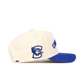 The No Rivals "Right Side Up CREIGHTON Hat - Classic Colors" is a cream cotton-canvas cap with a structured fit, blue brim, blue jay logo embroidery, letter C on the side, and CREIGHTON on the front.