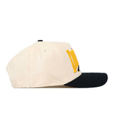 A side-profile view of the No Rivals Kennesaw State Stride Hat showcases its cream-colored crown with a black brim. Partially visible yellow embroidered letters on the side highlight its bold logo.