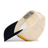 The Kennesaw State Stride Hat by No Rivals is shown flipped upside down, revealing its cream color, contrasting black brim, yellow side stitching, an interior label featuring the “NO RIVALS” text and a visible QR code, along with a classic snap back closure for adjustable fit.