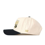 A white Colorado Buffaloes Stride Hat by No Rivals, featuring a black brim and crafted from high quality cotton for comfort and durability. This structured snapback cap showcases gold “NR” embroidery on the side, with additional text and logo on the front. The hat is photographed from the side against a white background.