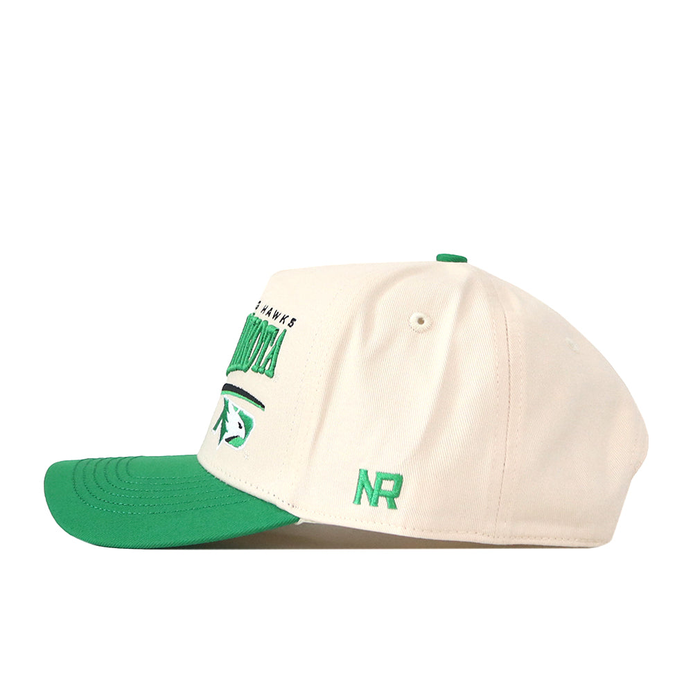 A side-angle view of the North Dakota Fighting Hawks Stride Hat by No Rivals, featuring a cream snapback design with a green brim, green NR initials embroidered on the side, and officially licensed North Dakota text and logo in green on the front.