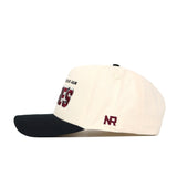 The Texas A&M Alma Mater Hat by No Rivals is a white cotton snapback with a black brim, maroon embroidered NR on the left, and partially visible maroon and black text on the front.