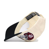 The Texas A&M Alma Mater Hat by No Rivals is a cream and black snapback, shown upside down to display its NO RIVALS tag. The front features a maroon patch with a white football helmet and ATX lettering, made from high quality cotton.