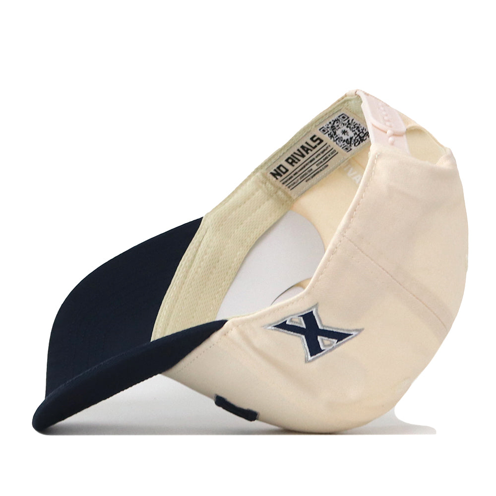 The Right Side Up Xavier Hat - Classic by No Rivals is displayed upside down, showcasing its beige and navy color scheme with a blue embroidered X logo on the side and an inner tag that reads NO RIVALS. This classic gameday cap offers a comfortable snap back adjustment for both comfort and style.