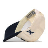 The Right Side Up Xavier Hat - Classic by No Rivals is displayed upside down, showcasing its beige and navy color scheme with a blue embroidered X logo on the side and an inner tag that reads NO RIVALS. This classic gameday cap offers a comfortable snap back adjustment for both comfort and style.