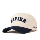 Sure! Here’s the rewritten sentence using your product data: The Right Side Up Xavier Hat - Classic by No Rivals features a beige base with a bold, navy embroidered “XAVIER” logo on the front and a contrasting navy brim. “NO RIVALS” is subtly stitched on the side, offering a classic gameday fit.