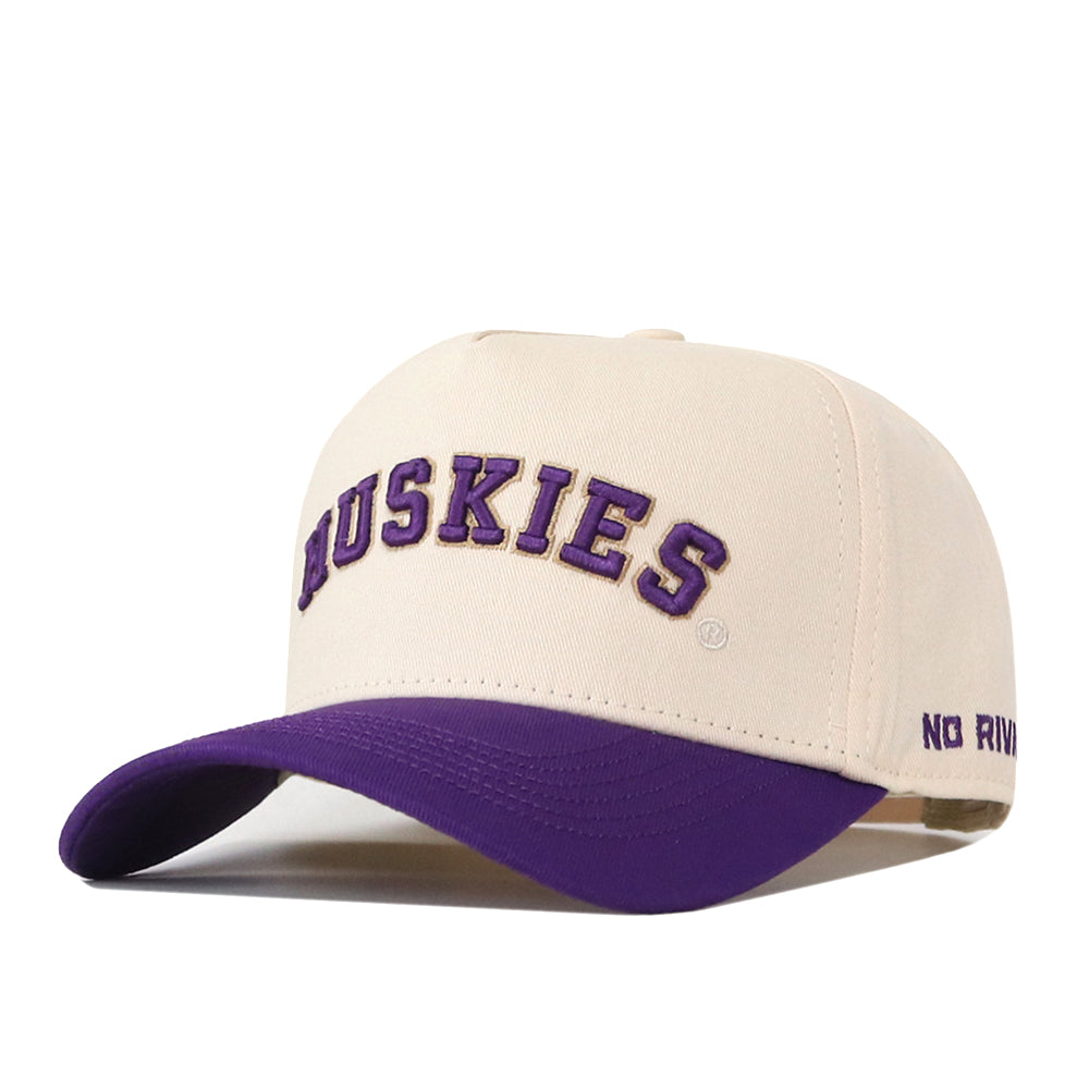 Introducing the Right Side Up Huskies Hat - UW - Classic by No Rivals: This beige baseball cap features a striking purple brim. “HUSKIES” is officially licensed and embroidered in bold purple letters on the front, while “NO RIV” is stitched in purple on the side. The hat includes a snap back adjustment for a comfortable fit.