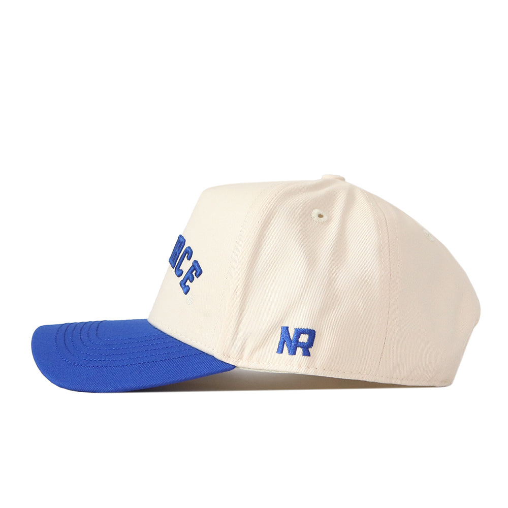 The Right Side Up Air Force Hat - Classic Colors by No Rivals features a cream-colored design with a blue brim, blue embroidered NR letters on the side, and partially visible blue text on the front. This cap includes an embroidered logo, stitched ventilation holes, and a snap back adjustment for comfortable wear on gameday.