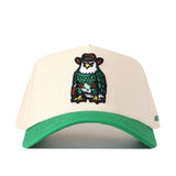 The UNT Desert Scrappy Logo Hat by No Rivals is a beige and green snapback cap made from a comfortable cotton blend. It features detailed patch embroidery of an owl wearing a cowboy hat and boots on the front, adding a playful touch to this stylish accessory.