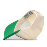 The UNT Desert Scrappy Logo Hat by No Rivals is a cream and green snapback, shown flipped upside down to reveal its interior label with a QR code and the NO RIVALS text. Made from a comfortable cotton blend, this cap offers extra style with patch embroidery details.