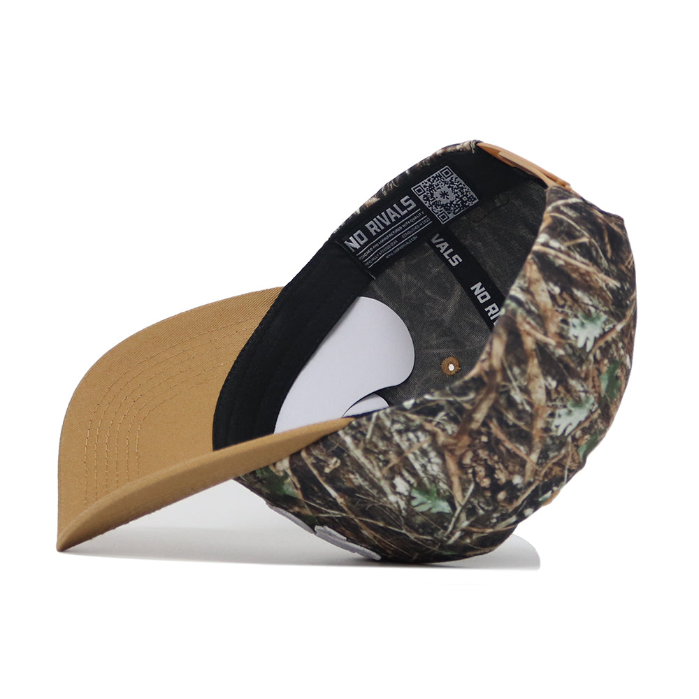 The Scheels Camo Explorer Hat is shown on its side, highlighting the inside label and black sweatband. It features a brown brim and a crown with a green, brown, and tan camo pattern.