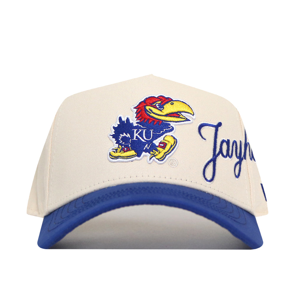 The No Rivals Kansas Jayhawks Halftime Hat is a beige and blue snapback featuring the University of Kansas Jayhawk logo embroidered on the front, with “Jayhawks” stitched in blue on the brim. This officially licensed cap boasts high-quality embroidery for a classic, spirited look.