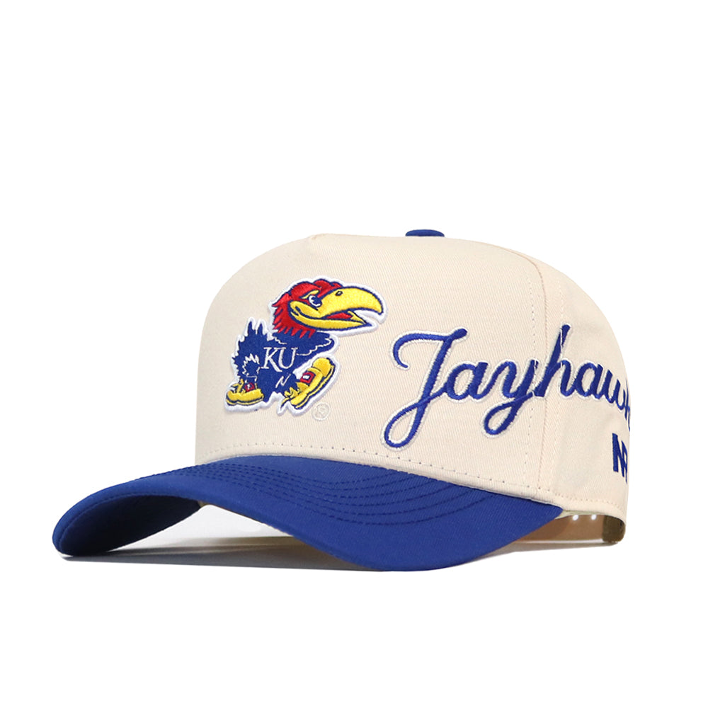 The No Rivals Kansas Jayhawks Halftime Hat is a beige and blue snapback cap featuring the KU Jayhawk mascot and "Jayhawks" embroidered on the front. This officially licensed hat showcases vibrant embroidery, making it perfect for true fans.