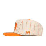 The Tennessee Pinstripe Traditions Hat by No Rivals features a cream-colored design with thin orange vertical stripes, an orange flat brim, a large embroidered orange logo on the front, and orange “NR” initials on the side. Crafted from a soft cotton blend with a snap back closure for an adjustable fit, this cap is displayed in a left side profile view.