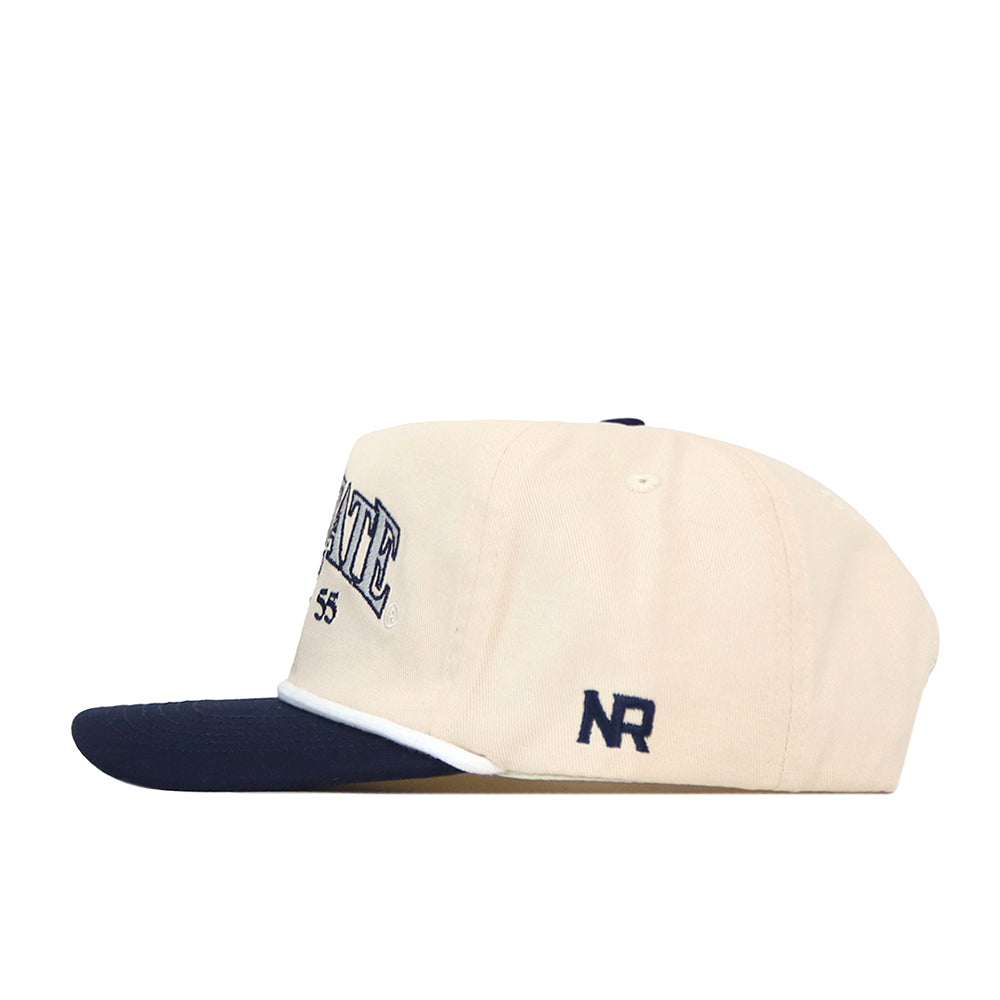 A beige Penn State Vintage Block Hat by No Rivals, featuring a navy blue brim, an embroidered NR logo in navy on the side, and part of the STATE 1955 text on the front. This officially licensed hat offers a snap back adjustment for a comfortable fit.