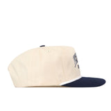 A side view of the Penn State Vintage Block Hat by No Rivals showcases its cream-colored snapback design with a navy blue brim. The hat features an embroidered logo, a small button on top, and partially visible text on the front panel. This officially licensed snapback is ideal for fans who value both quality and style.