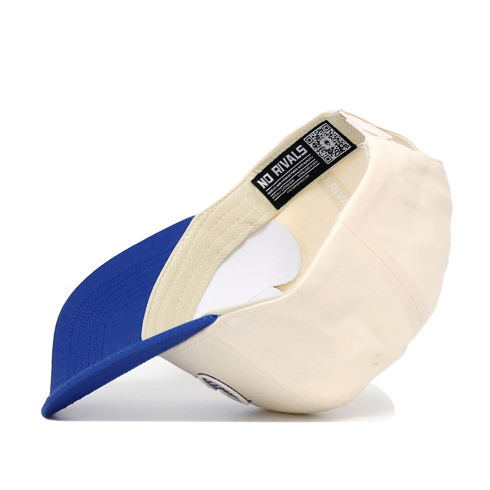The Creighton Triangle Game Cap Hat by No Rivals is shown upside down, revealing its cream color, blue brim, and an inside label with the NO RIVALS brand name and a QR code.