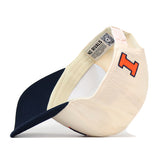 A cream and navy Illinois Fighting Illini Stadium Hat by No Rivals featuring a red and blue embroidered “I” logo on the front. The snapback hat is shown flipped to display its interior label and adjustable strap, emphasizing its quality as an officially licensed product.