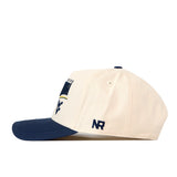 A structured fit WVU Mountaineers Stride Hat by No Rivals, featuring a cream-colored crown, navy blue brim, and embroidered NR initials on the side, crafted from high-quality cotton and displayed in side profile against a white background.