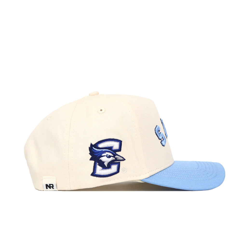 The No Rivals Upside Down JAYS Hat - Creighton - Light Blue is a cream cap with a light blue brim, featuring a blue jay logo, embroidered details, and the letter C on the side. Officially licensed with a structured fit.