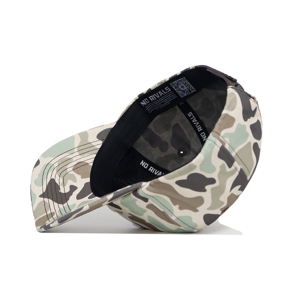 The Nebraska Huntsman Hat by No Rivals is displayed upside down, showing its interior and the NO RIVALS label on the band. The 5-panel crown and brim feature a beige, green, and brown camo print.
