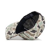 The Nebraska Huntsman Hat by No Rivals is displayed upside down, showing its interior and the NO RIVALS label on the band. The 5-panel crown and brim feature a beige, green, and brown camo print.