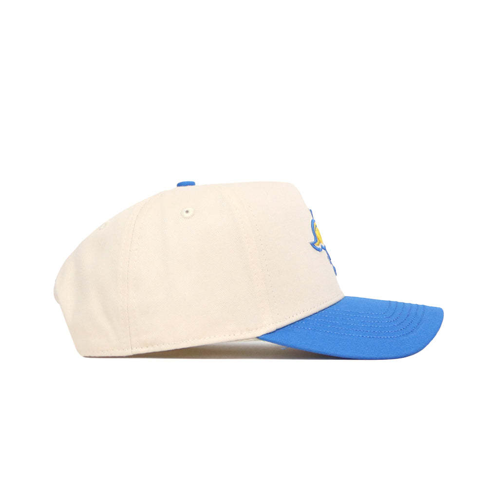 The No Rivals South Dakota State Logo Patch Hat is a cream structured-fit baseball cap with a blue curved brim and a small embroidered yellow and blue detail on the side. Shown in side profile, this snapback is set against a white background.
