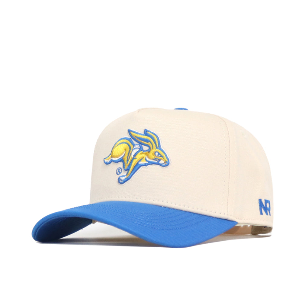 The South Dakota State Logo Patch Hat by No Rivals is a cream structured baseball cap with a blue brim, featuring an embroidered yellow and blue jackrabbit logo on the front and NR letters on the side—perfect for any occasion.