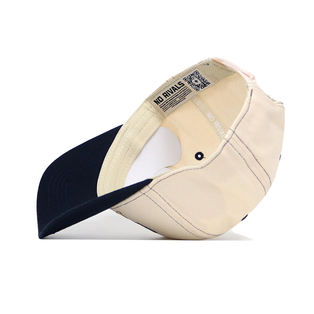 The ETSU Vintage Hat by No Rivals is shown upside down on a white background, revealing its inside stitching, NO RIVALS label, and a QR code on the inner band. This beige and navy snapback offers a structured fit in high quality cotton.