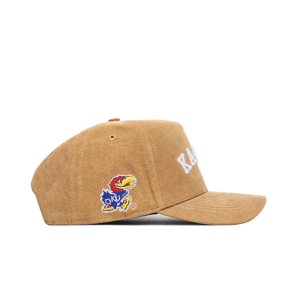 The No Rivals Kansas Rustic Hat is a tan cotton canvas hat with "KANSAS" in white on the front and the University of Kansas Jayhawk logo on the side, shown in a side profile view against a white background.