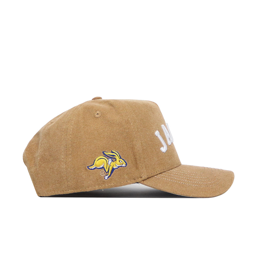 The No Rivals South Dakota State Rustic Hat is a brown cotton canvas snapback with a structured fit, “JACKS” embroidered on the front, a yellow and purple jackrabbit logo on the side, and a curved brim. Displayed on a white background.
