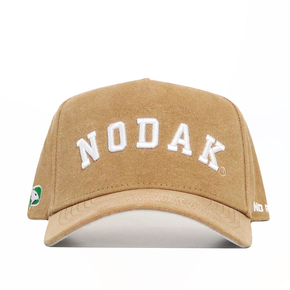 The North Dakota Rustic Hat by No Rivals is a tan cotton canvas cap with "NODAK" in bold white letters, a green and white patch on the left side, and small white text on the right brim. Structured fit for style and comfort.