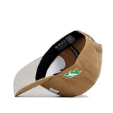 The North Dakota Rustic Hat by No Rivals is a tan cotton canvas cap with a curved brim, white underside, and green arrow design. It features NO RIVALS text, a QR code inside, and is shown propped on its side.