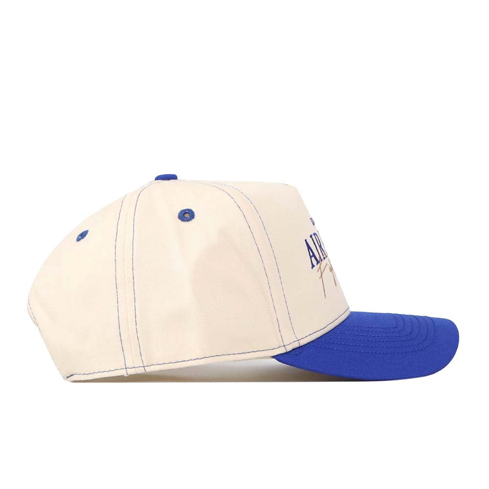 A side view of the No Rivals Air Force Vintage Hat is shown on a white background. This structured cap features a cream-colored crown with blue stitching and a matching blue brim, and is crafted from high-quality cotton.