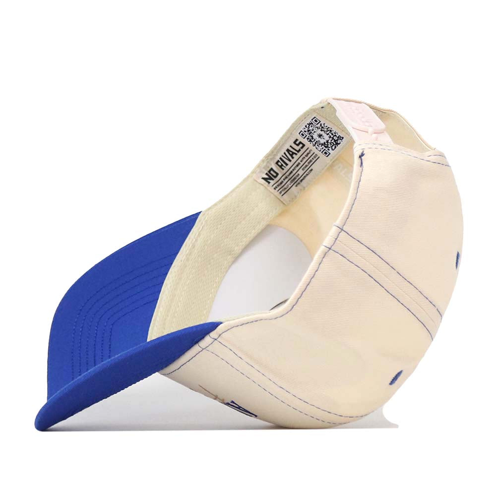 The No Rivals Air Force Vintage Hat is a cream and blue baseball cap shown from the side, with the signature NO RIVALS inside label visible. This snap back hat features a curved blue brim and cream-colored panels accented by detailed stitching, offering a structured fit crafted from high-quality cotton.