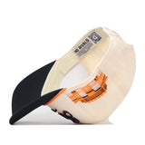 A Tennessee Old Script Neyland Hat by No Rivals is pictured upside down. The inside label displays the No Rivals brand, while the front showcases an orange and black graphic design with buildings. A QR code can be seen on the inner lining.