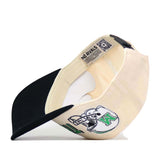 The Marshall Alma Mater Hat by No Rivals is featured here in cream and black, shown upside down to display its interior labels and a skull graphic adorned with a green K on the side. This licensed snapback cap offers a structured fit and is crafted from high-quality cotton for comfort and durability.