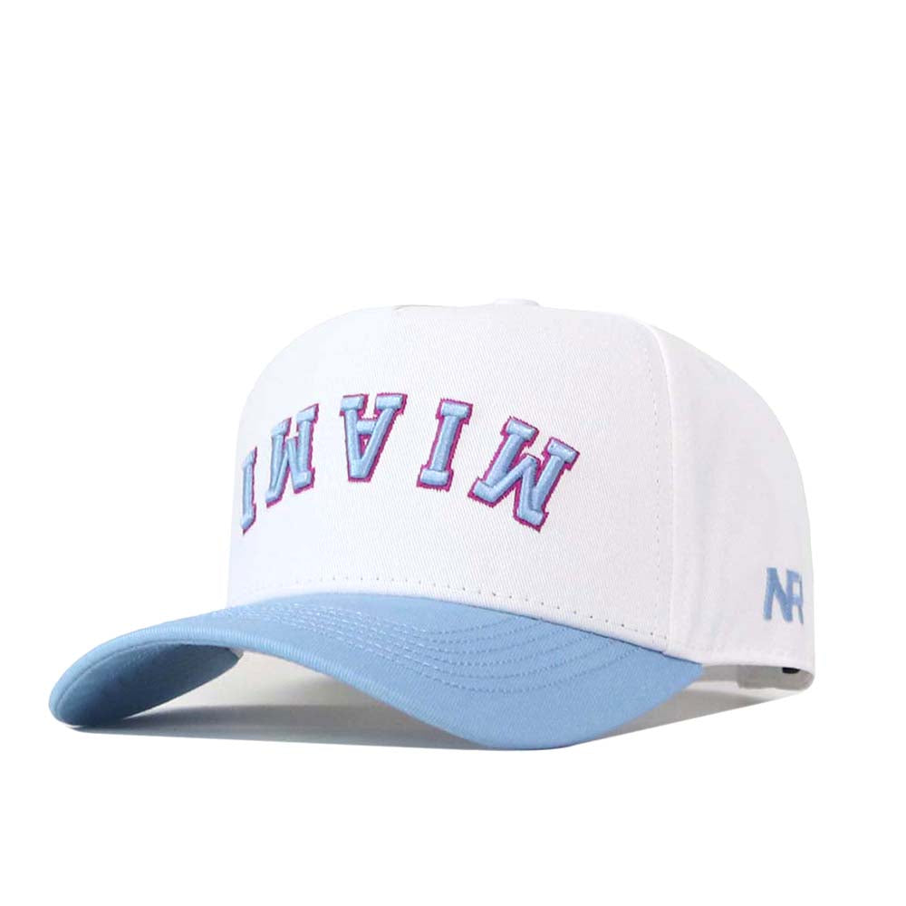 The No Rivals FIU Panthers | Upside Down Miami Hat - Whiteout is a white snapback cap with a light blue brim, featuring “MIAMI” embroidered upside down in pink and blue letters on the front.