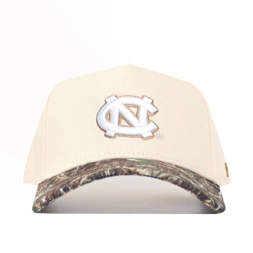 The No Rivals UNC Camo Connector Hat features a beige snapback design, the University of North Carolina interlocking NC logo on the front, a camo-patterned brim, and is crafted from high-quality cotton for structure and style.